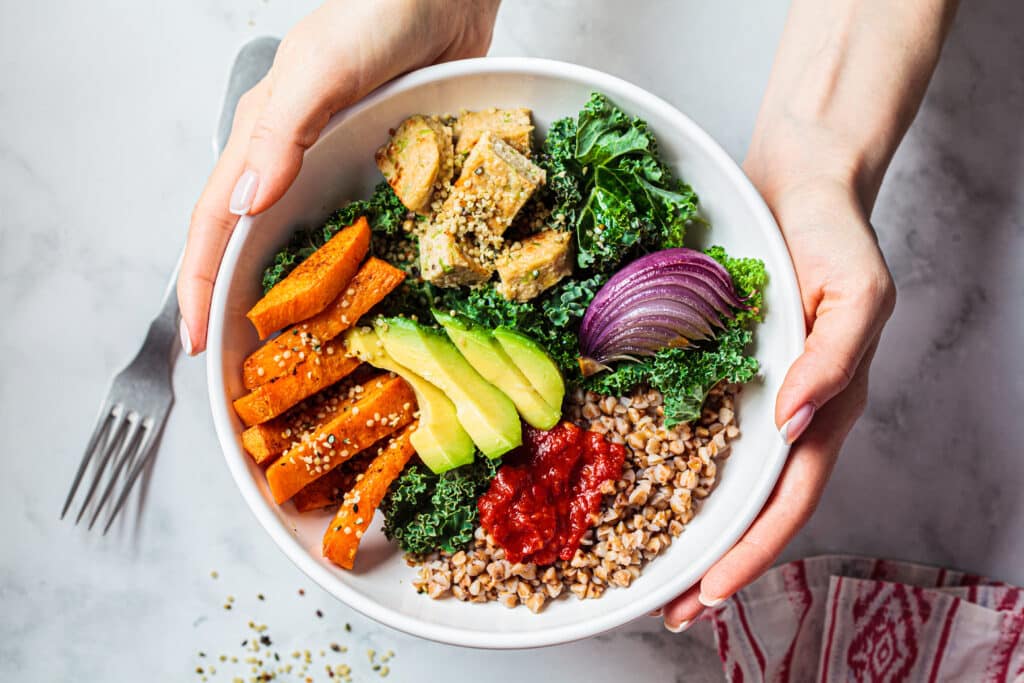 Woman hands eating vegan salad of baked vegetables, avocado, tof